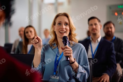 Preview: Female entrepreneur speaking into microphone from the audience during a business seminar.
