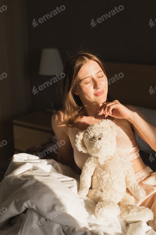 Preview: Portrait of girl is waking up in morning stretches in bed and sun shines from window. Happy young