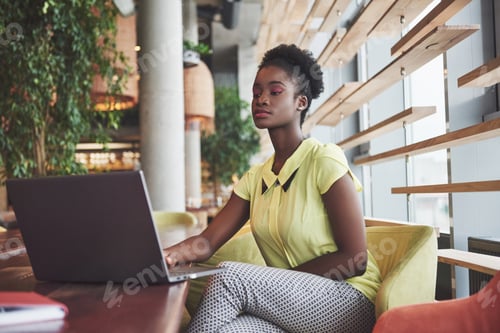 Preview: Beautiful young woman sitting in a cafe and working on a laptop