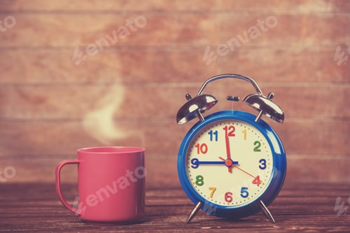 Preview: Cup of coffee and alarm clock on wooden table.