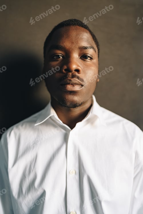Preview: Close up portrait of young african man in white shirt against black wall in studio