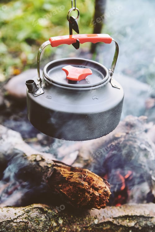 Preview: Outdoor camping kettle suspended over open fire in natural setting