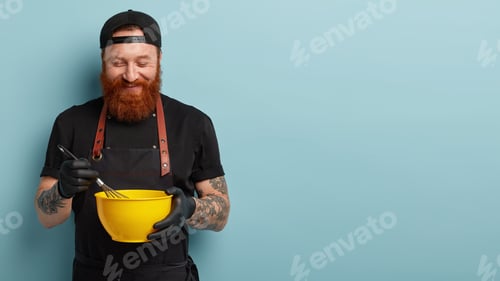 Preview: Satisfied chef mixes ingredients in bowl with whisk, holds kitchenware, prepares delicious dish, wea
