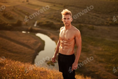 Preview: Confident fit shirtless sportsman looking at camera while standing on hill slope