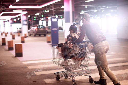 Preview: ✓ Cheerful happy young couple in casual clothes having fun and riding on a shopping cart