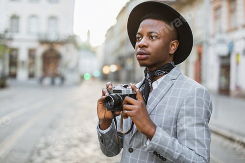 Preview: African man taking photo on retro camera while walking