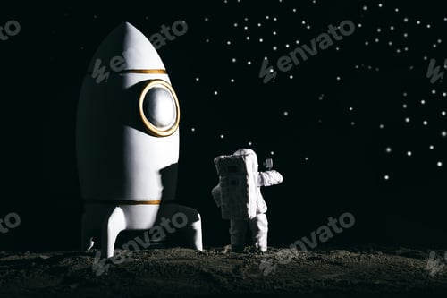 Preview: Astronaut miniature toy next to a rocket on the moon against bokeh background