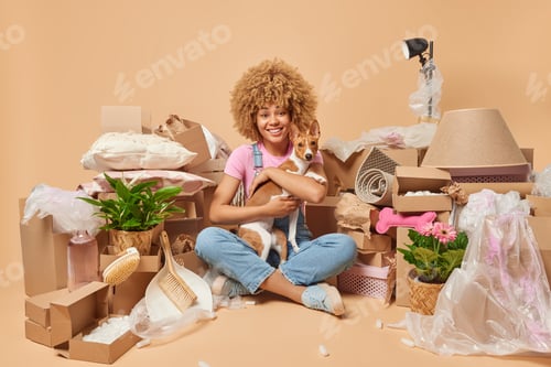 Preview: Relocation day concept. Positive curly haired woman embraces favorite pet move together to new apart