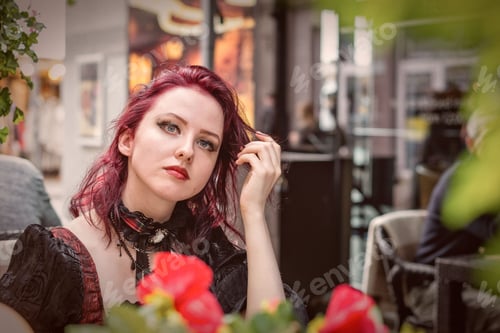 Preview: Young gorgeous redheaded woman sitting in an outdoor cafe dressed in retro fashion clothes.