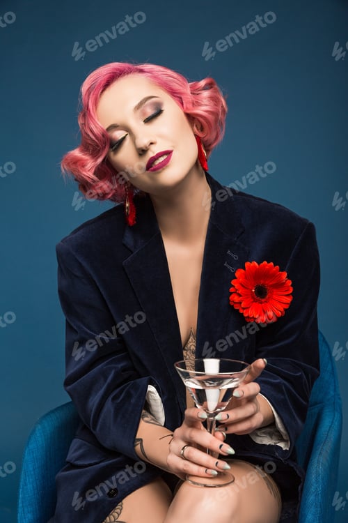 Preview: beautiful tattoed pin up girl in jacket with boutonniere and wineglass infront of blue background
