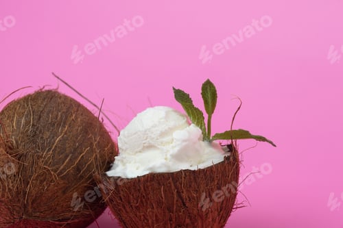 Preview: Vanilla ice cream balls in fresh coconut halves decorated with mint leaves on a pink background