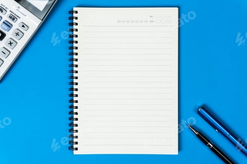 Preview: Open notebook with calculator and pen from top view on blue background.
