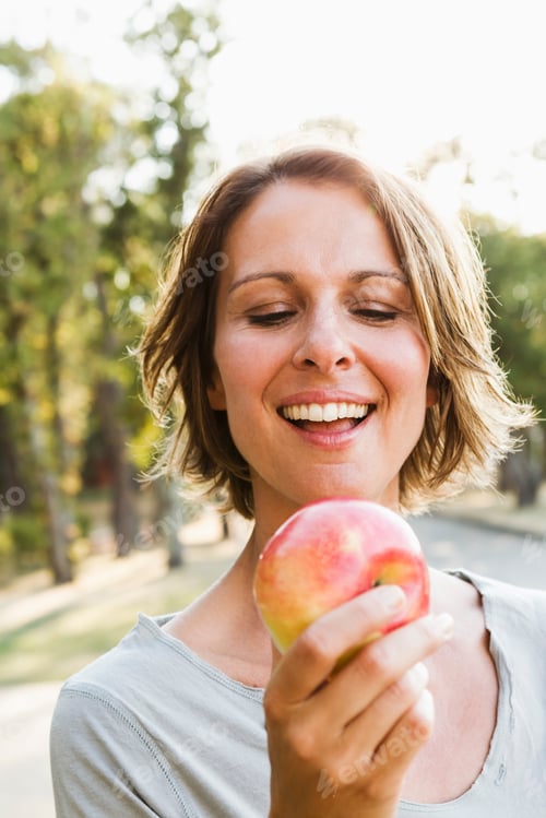 Preview: Smiling woman eating apple outdoors