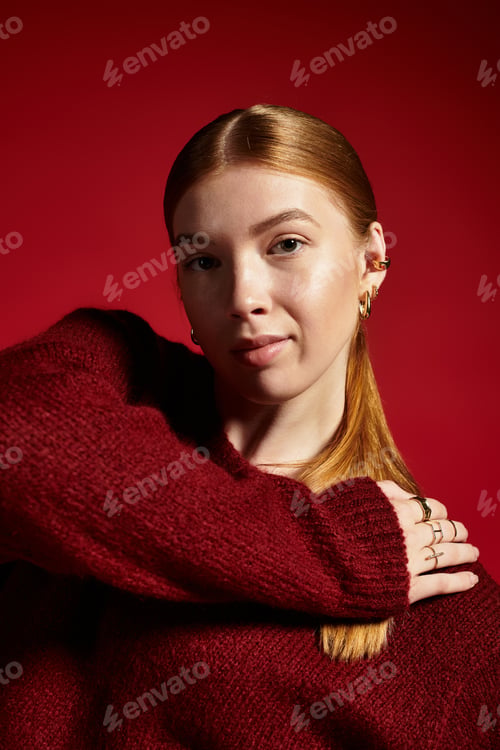 Preview: Young woman with red hair showcases cozy winter style against a vibrant backdrop