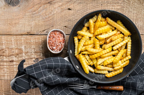 Preview: Fried Crinkle oven French fries potatoes sticks in a pan. Wooden background. Top view. Copy space