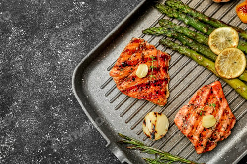 Preview: Frying pan with tasty grilled salmon, lemon and asparagus on black table, top view. Space for text