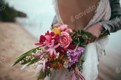Preview: Cropped View of Bride and Groom Holding Wedding Bouquet and Embracing on Beach
