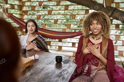 Preview: smiling african american woman meditating near girlfriends and tea cups on wooden table