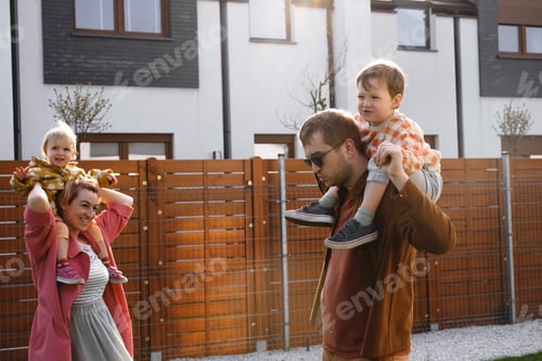 Aperçu: Mother father carrying kids on piggyback near house on sunset