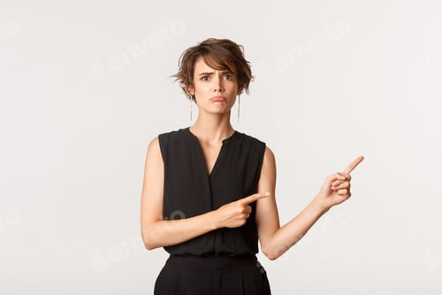 Preview: Sad young woman complaining, pointing fingers right at banner and sulking upset, white background