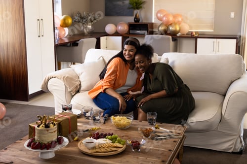 Preview: Celebration at home, friends laughing and eating snacks and cake on sofa