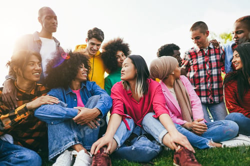 Preview: Multiethnic diverse people having fun outdoor sitting on grass at city park
