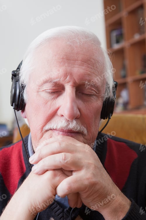 Preview: Senior man listening to music on earphones at home