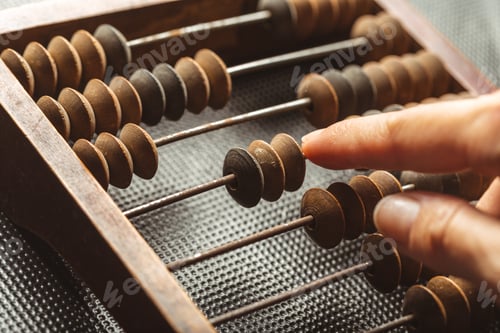 Preview: Finger touches a wooden bead on a vintage abacus in a quiet setting during the day