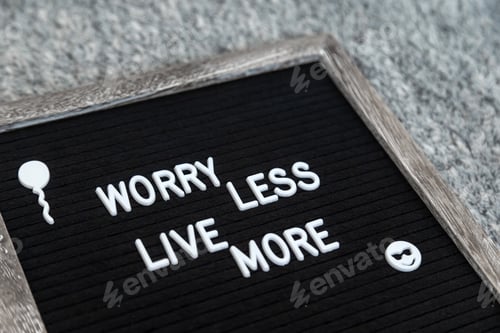 Preview: Felt letter board sign "Worry less, live more" in a wooden frame on black background. Closeup.