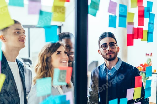 Preview: Joyful employee reading notes on glass wall with coworkers