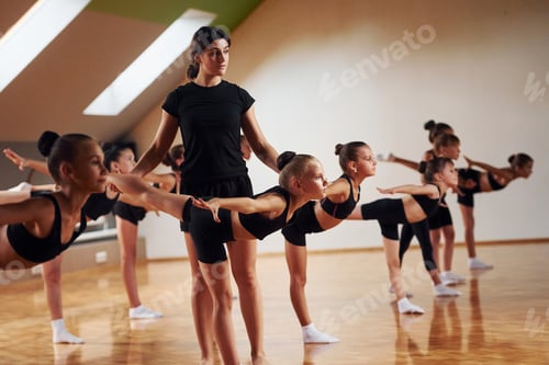 Preview: Coach is helping. Group of female kids practicing athletic exercises together indoors