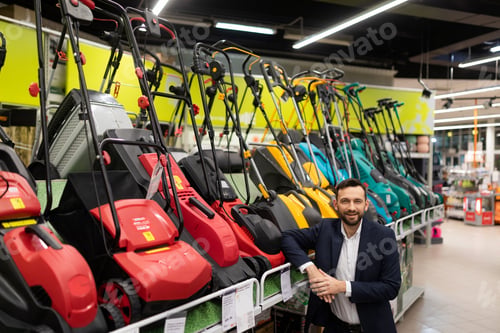 Preview: Owner of a gardening power tool store next to a display case with rechargeable electric lawn mowers
