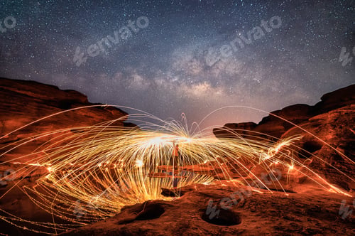 Preview: Man wielding spark fire swirl on rock canyon and holes with milky way in the night sky