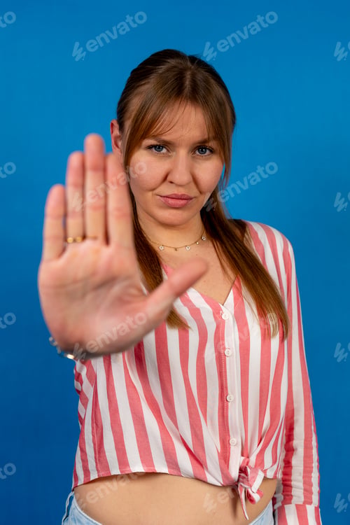 Preview: Serious young woman making stop sign with hand on blue background