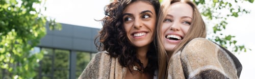 Preview: happy lesbian couple covered in blanket laughing in park, banner