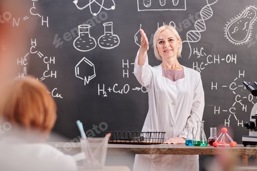 Preview: Blond cheerful teacher of chemistry in whitecoat pointing at one of schoolkids