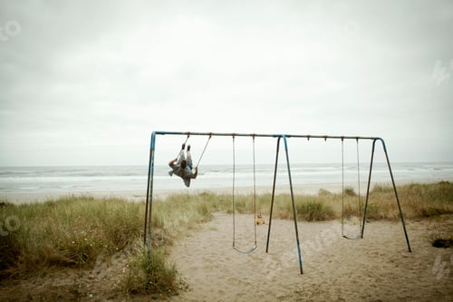 Preview: Female toddler watching father on beach swing