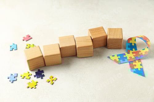Preview: Ribbon with colorful puzzle pieces and wooden cubes on light background. World autism day concept