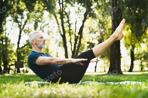 Preview: Mature handsome man in sporty clothes doing workout practicing yoga fitness outdoors outside in park