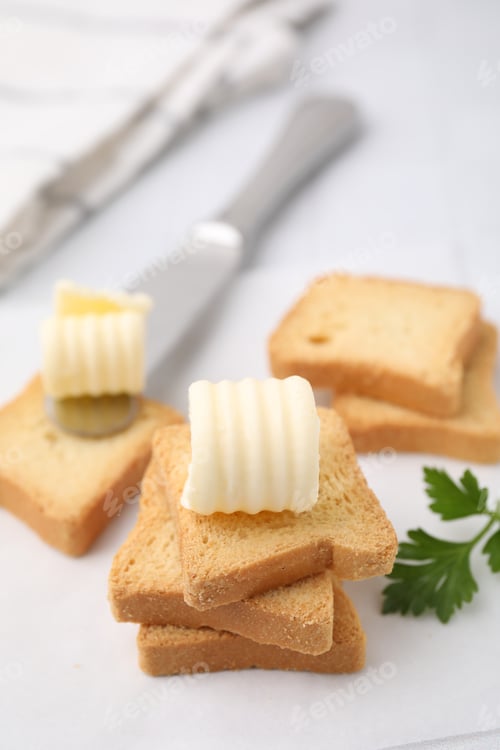 Preview: Tasty butter curls, knife and pieces of dry bread on white table, closeup