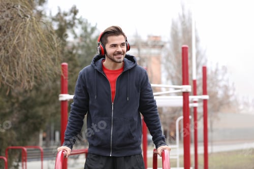 Preview: Young man with headphones listening to music and exercising on sports ground