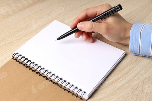 Preview: Female hand writes in blank notebook on wooden table
