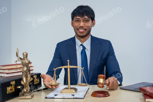 Preview: An Asian businessman in a formal suit works alone at a lawyer's desk, by golden scales, law books