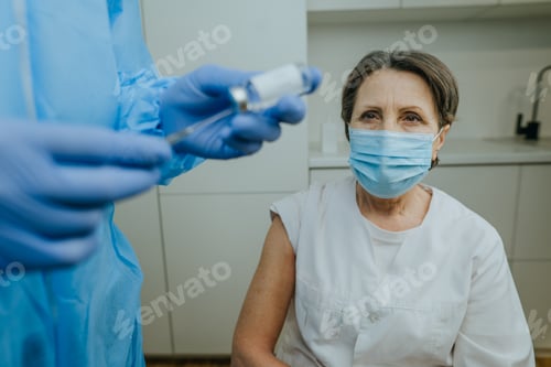Preview: Mature woman healthcare worker waiting for COVID-19 vaccination at hospital. Doctor in protective ov