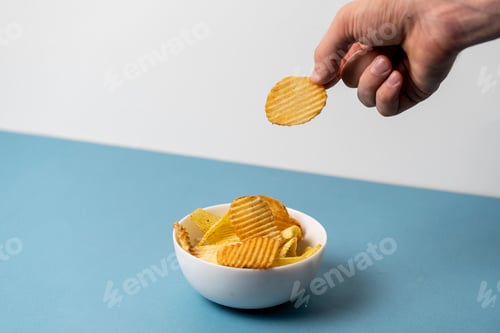 Preview: simple concept of junk food, hand pick a single potato chip from bowl