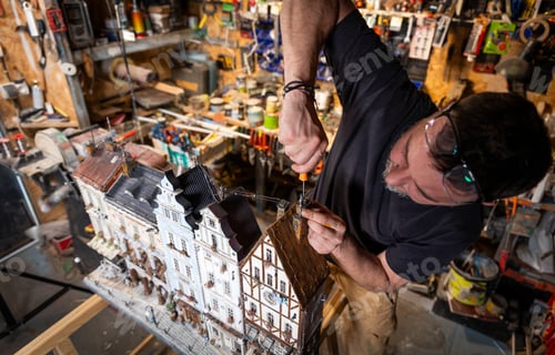 Preview: Model maker man working at scale model of miniature building in his workshop full of tools