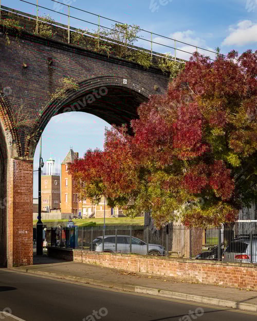 Preview: Brick railway viaduct with autumn trees in cityscape.