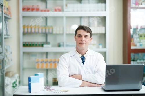 Preview: Male pharmacist working in modern pharmacy using laptop.
