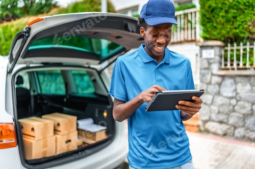 Preview: African delivery man using digital tablet standing next to van