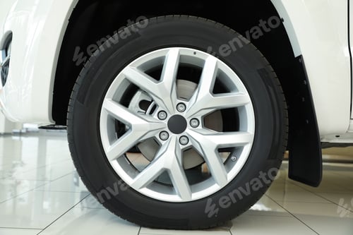 Preview: Wheel of new luxury white car in modern auto dealership, closeup